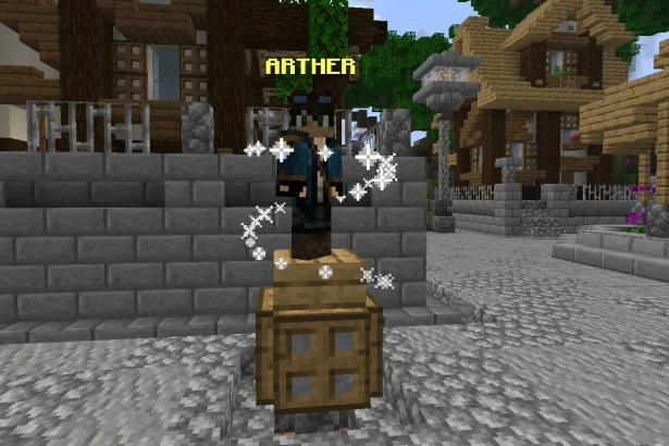 A Minecraft screenshot of the NPC Arther standing on a wooden crate pedestal in a cobblestone town square. Arther wears a blue adventurer's jacket and goggles, surrounded by swirling white magical particle effects. Rustic wooden buildings and a street lamp are visible in the background.