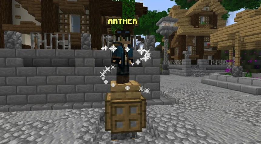 A Minecraft screenshot of the NPC Arther standing on a wooden crate pedestal in a cobblestone town square. Arther wears a blue adventurer's jacket and goggles, surrounded by swirling white magical particle effects. Rustic wooden buildings and a street lamp are visible in the background.